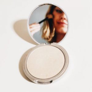 Small image of a woman applying makeup looking into her compact mirror