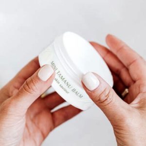 Image of two hands holding a small jar of Tropic Tamanu Balm, a skin saviour product from the Tropic Skincare range